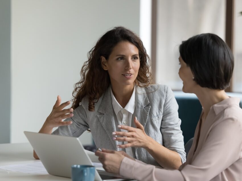 Two,Business,Women,Sit,At,Desk,Discuss,Project,Details,,Diverse